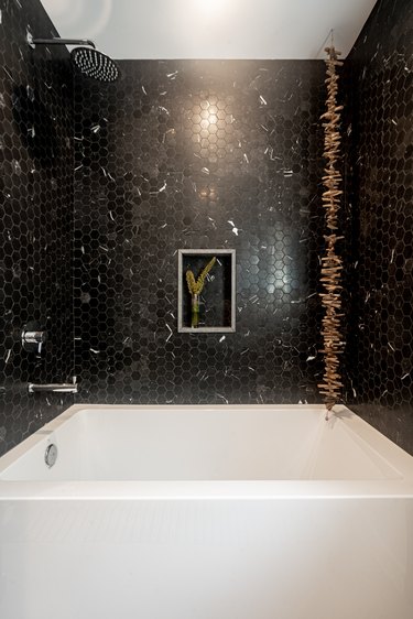 Black penny tile wall around white bathtub