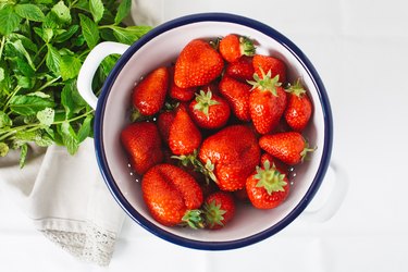 strawberries in ceramic bowl next to fresh green herbs