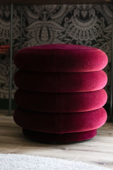 ferm LIVING jewel-tone round pouf next to patterned wallpaper