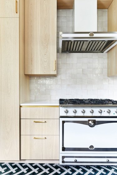 light wood cabinets with patterned tile floor and textured backsplash and brass hardware