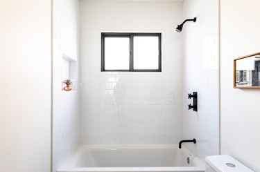 white bathroom with subway wall tile, black showerhead and faucets, white dual flush toilet