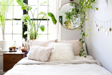 Boho bedroom with blush and off-white textured bedding, several plants, and round wall mirror