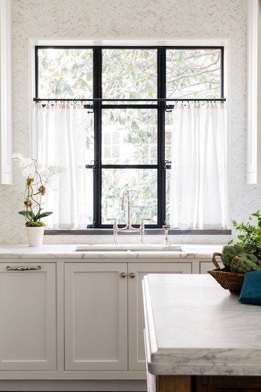 Modern kitchen window with half curtains and marble island