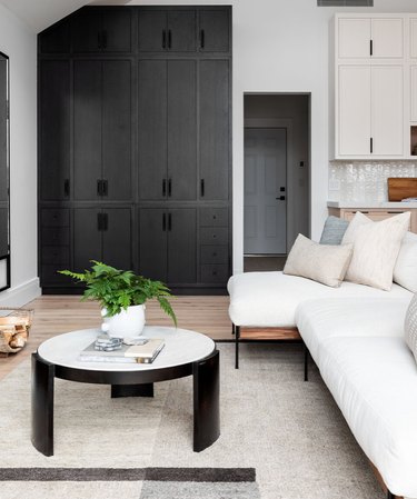 basement storage ideas with black built-in cabinets, white sectional couch, throw pillows, white and black round coffee table, geometric rug.