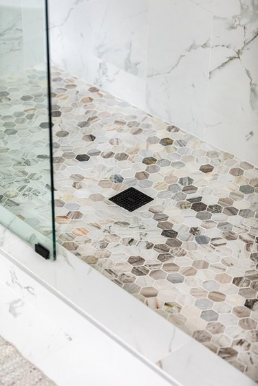 black shower drain, multicolored hexagon shower floor tile, marble wall tile, glass shower door