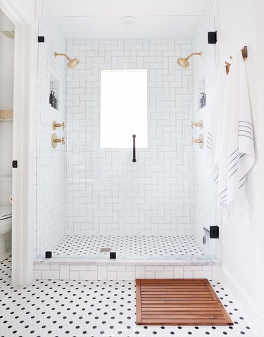 white tile shower with gold fixtures and black accents on the tile floor