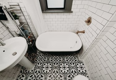 black and white tile patterned floor, freestanding black and white clawfoot tub, white subway tile wall, bronze wall-mount faucet, white pedestal sink