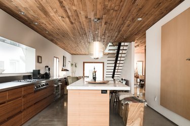 wood kitchen, wood kitchen island with white stone countertop and dark wood-paneled ceiling with hanging pendant lights