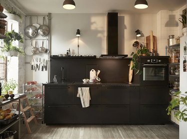 black kitchen cabinet idea for an industrial loft kitchen with black lower cabinets, a black blacksplash, and a black range hood
