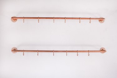 Two copper pipes with S hooks mounted on wall