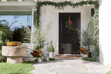 black traditional front doors with green garland and potted plants