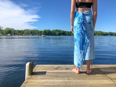 Woman wrapped in tie-dye towel by lake