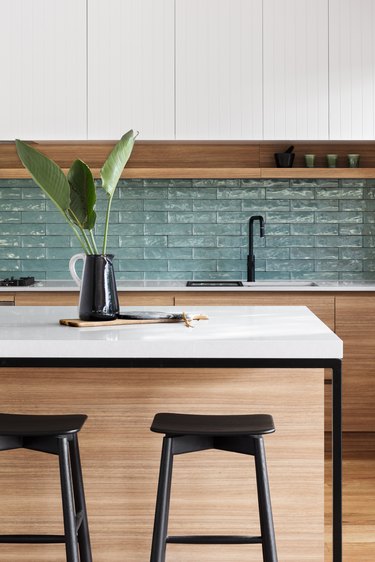 green textured kitchen backsplash with wood cabinetry and whit countertops