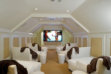 attic game room with white chaise loungers, yellow and white walls, big screen tv, white end tables, brown throws.