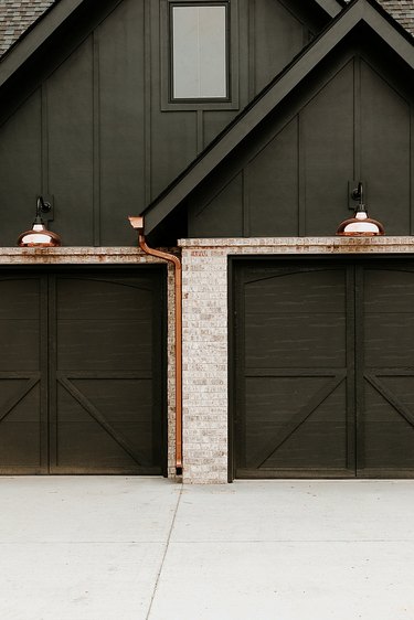 Exterior house lights in copper above garage doors of black exterior
