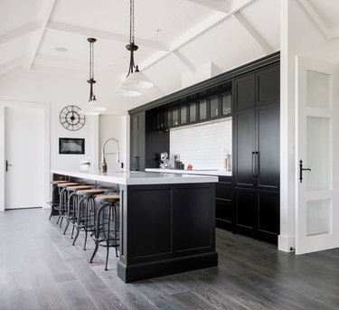 Black bar and cabinets with gray wood floor, white ceiling, industrial barstools, pendant lights in industrial basement
