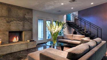 Concrete mantel, concrete floors, gray couches, fireplaces, stairway, large vase with flowers in industrial basement