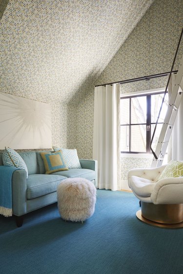 attic living room with blue sofa, rug, wallpaper and sheepskin pouf