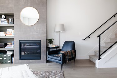 gray living room with gray wood floor and black armchair, fireplace and black stair rail