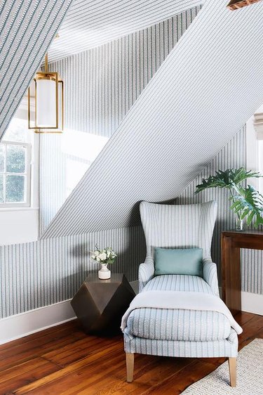Small attic ideas in a space with vertical lined wallpaper, matching lounge chair, and gold accent lamp.