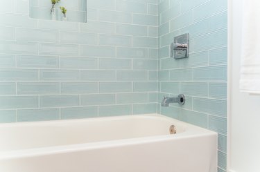 An alcove bathtub with light blue subway tile and a wall niche with two small plant vases