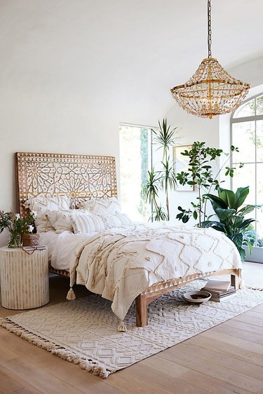 bedroom with handcarved wood headboard with plants and chandelier
