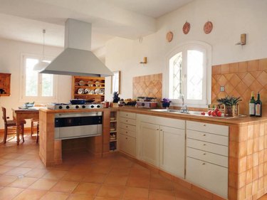 A desert-inspired kitchen with terra cotta tiles and white cabinets and a large extractor above the oven
