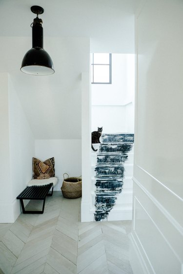 black and white stairs with abstract artwork using paint leading to entry way with chevron floors