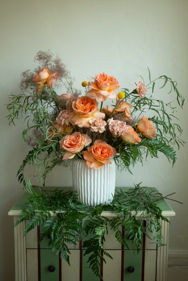 white vase with floral arrangement on top of striped furniture piece