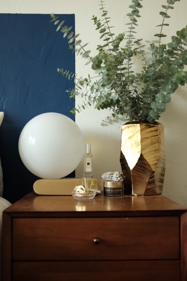 nightstand with lamp and gold vase with greenery