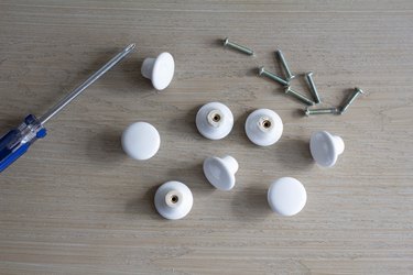 Eight white cabinet knobs with screws removed by screwdriver