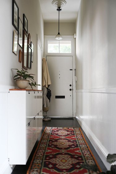narrow hallway with area rug, storage cabinet, and pendant light
