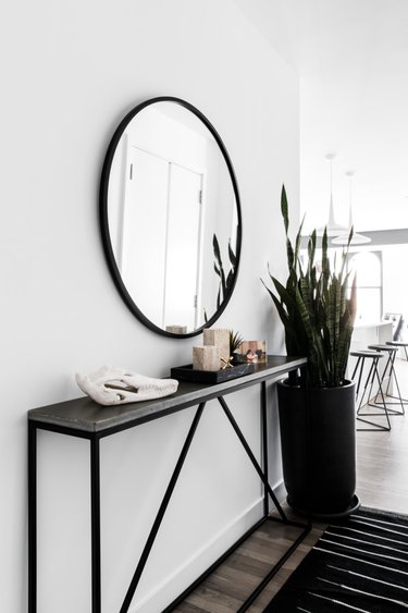 narrow console table in hallway with round mirror and area rug