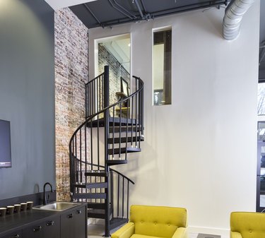 attic stairs ideas with black metal spiral staircase, yellow side chairs, brick wall.