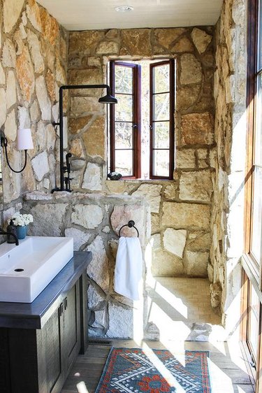 stone rustic shower tile in bathroom with white sink and black fixtures