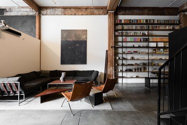 industrial pipe shelving in living room with gray sectional and leather chairs