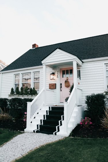 White farmhouse with stairs leading up to front door with black and white carpet.