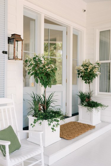 Farmhouse entryway with white planters, plants, white porch.