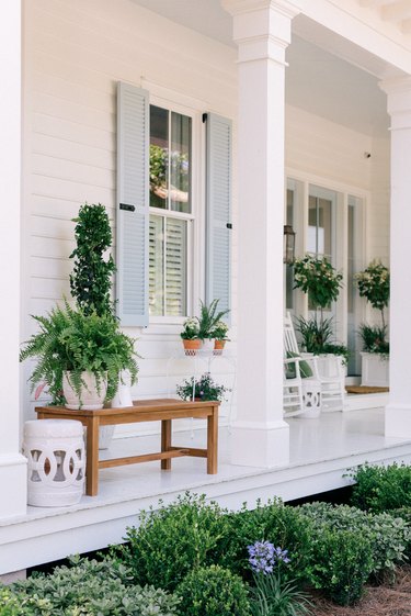 Blue exterior house shutters shown on white front porch with potted plants