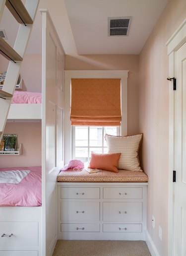 attic storage in girls bedroom with orange Roman shade and window seat