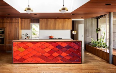 midcentury kitchen island idea with red tile back panel and wood cabinets