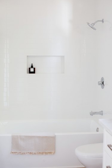 white tub with a fringed towel draped over, white shower wall