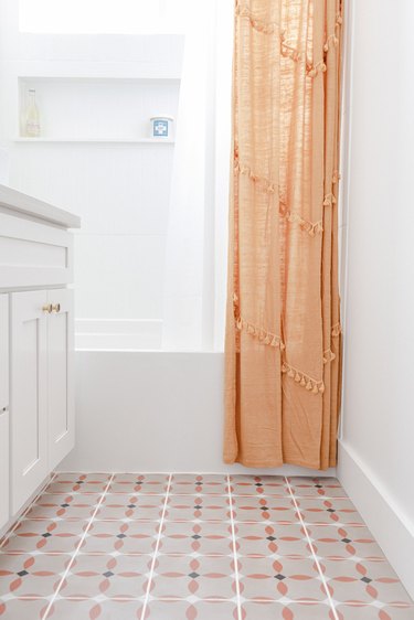 patterned floor tile, white bathroom vanity, orange shower curtain, white tub and shower surround