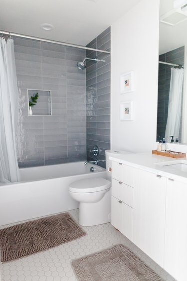 white hexagon floor tile, white bathroom vanity, white toilet, white tub with gray shower wall