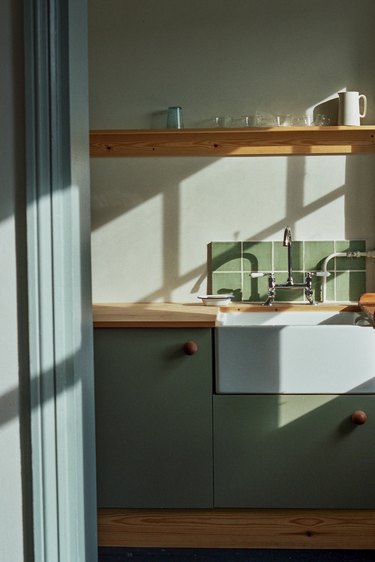 minimal sage green kitchen backsplash with green cabinets and wood countertop