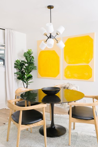 Dining room with mustard yellow abstract artwork on wall next to small dining table and chairs