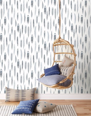 rattan hanging chair against blue and white feather coastal wallpaper