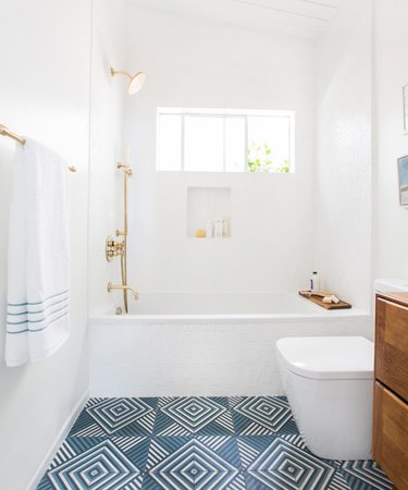 white coastal bathroom with blue geometric concrete tile floor, brass fixtures and natural wood vanity.