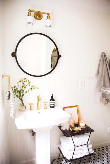 bathroom pedestal sink with round mirror above and black and white mosaic floor tile