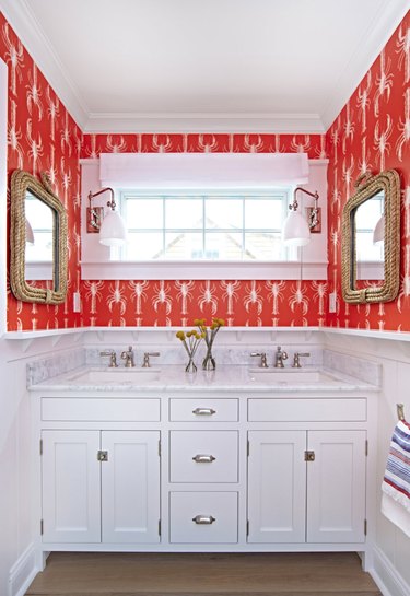 Marble coastal bathroom with his and her sinks with red lobster patterned wallpaper and rope frame mirrors.